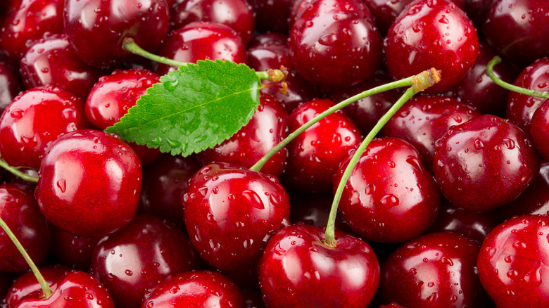 A pile of cherries, some with stems, one with a leaf.