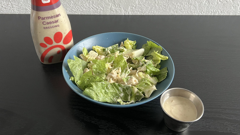Blue bowl of Caesar salad with bottle and cup of Chick-fil-A Parmesan Caesar dressing