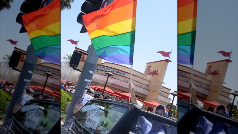Person lifting a rainbow pride flag from inside a vehicle at a protest outside Chick-fil-A.
