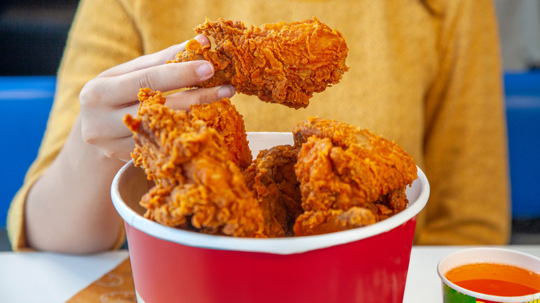 person eating bucket of crispy fried chicken