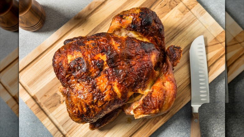 homemade roasted whole chicken with crispy skin on cutting board with knife