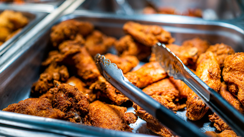A fried chicken buffet container with metal tongs