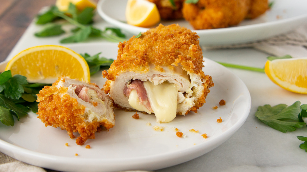 Chicken cordon bleu oozing cheese onto a white plate