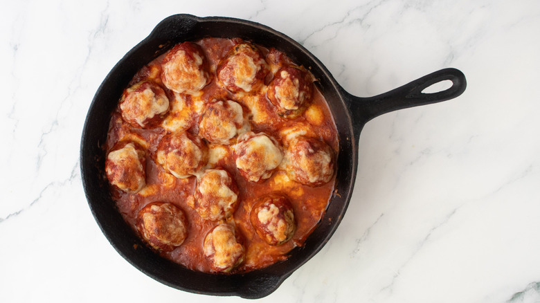 Sauced meatballs in skillet with melted cheese on top