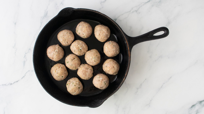 Uncooked chicken meatballs in skillet