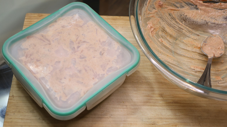 sealel container of marinating chicken thighs next to empty bowl