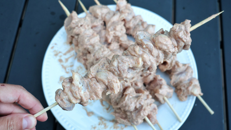 hand holding raw chicken skewer above plate of the same