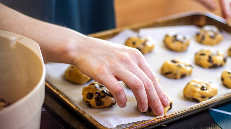 Hand pressing down on ball of cookie dough atop baking sheet