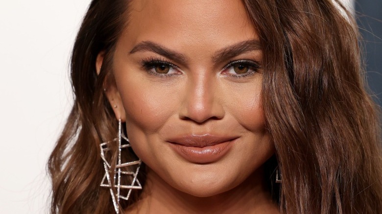 close up of chrissy teigen's face, wearing geometric silver statement earring