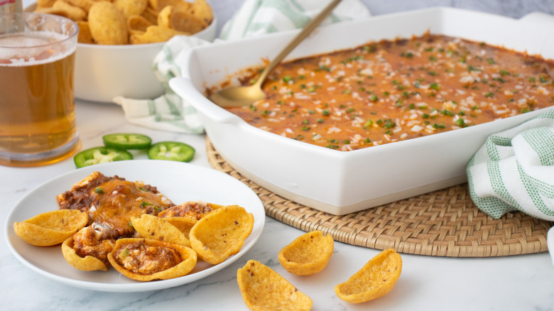 Fritos on plate topped with chili dip and casserole dish full of chili dip in background