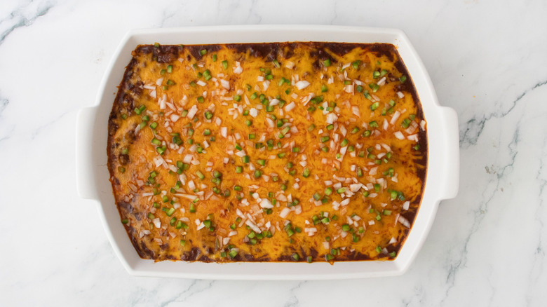 Chili dip topped with cheese, onion, and jalapeño in casserole dish