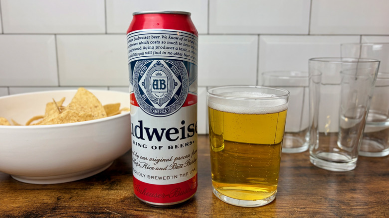 A red and white can of Budweiser beside a glass of beer