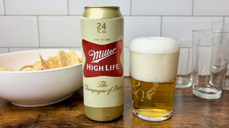 A Champagne-colored can of Miller High Life next to a glass of beer with a large frothy head