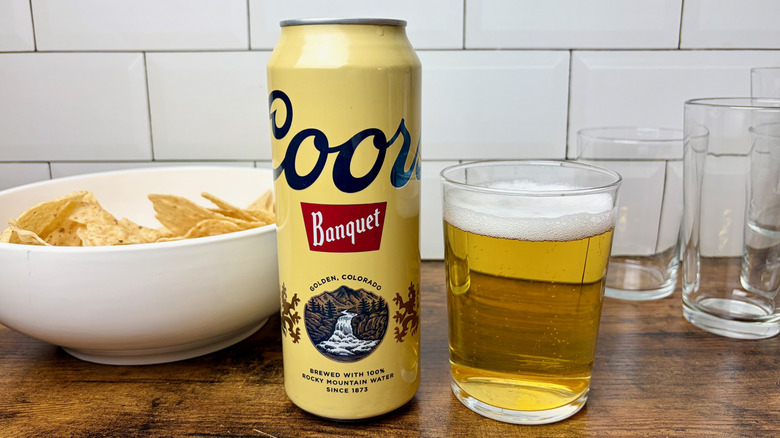 A yellow can of Coors Banquet beer beside of glass of beer