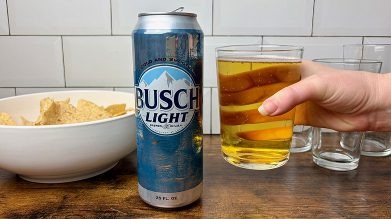 A blue can of Busch Light and a hand holding a glass of beer