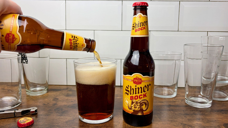 A bottle of Shiner Bock beer pouring into a glass, next to another bottle of Shiner Bock beer