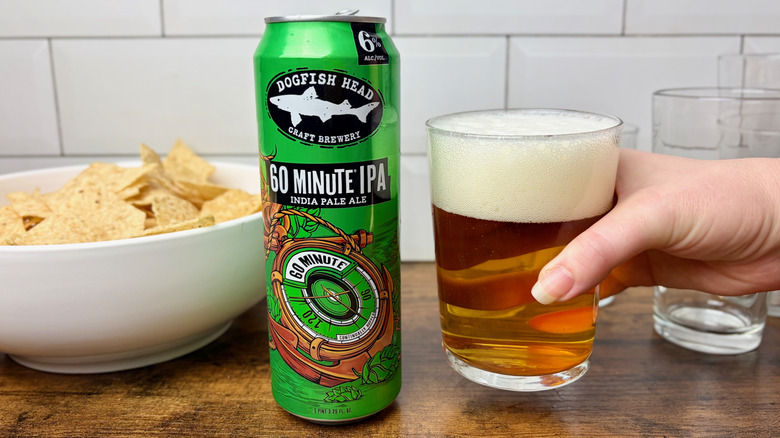 A green can of Dogfish Head 60 Minute IPA and a hand holding a glass of amber beer