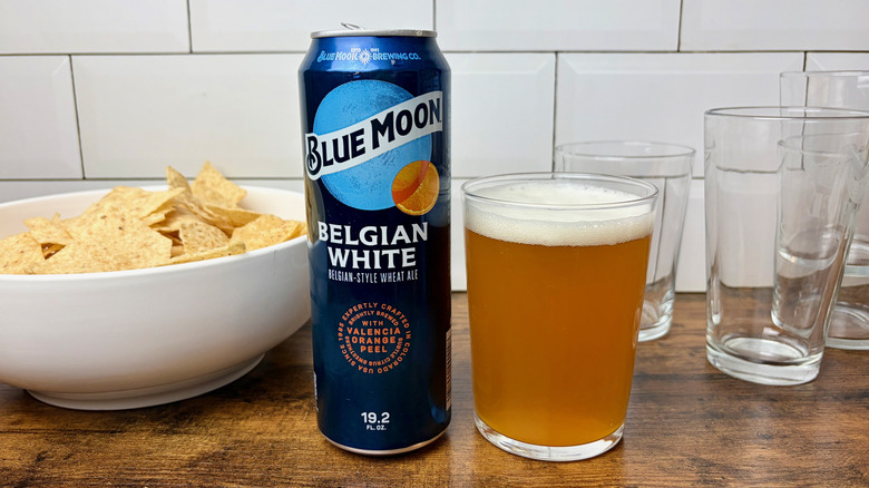 A blue can of Blue Moon Belgian White beer next to a glass of copper-color beer