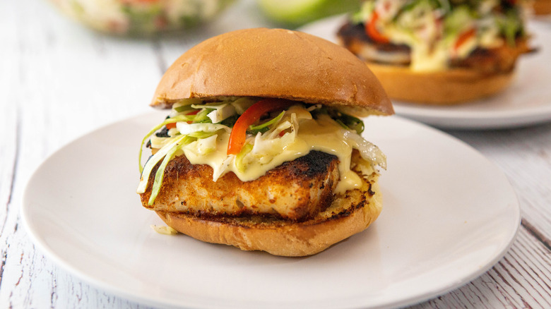 Blackened fish sandwich on a white plate with other sandwiches behind 