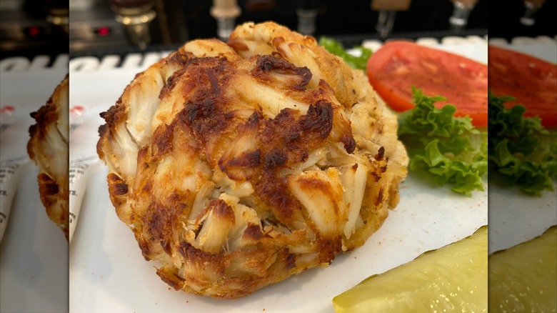A crab cake that has large chunks of crab and very little filler with a piece of lettuce and a slice of tomato next to it