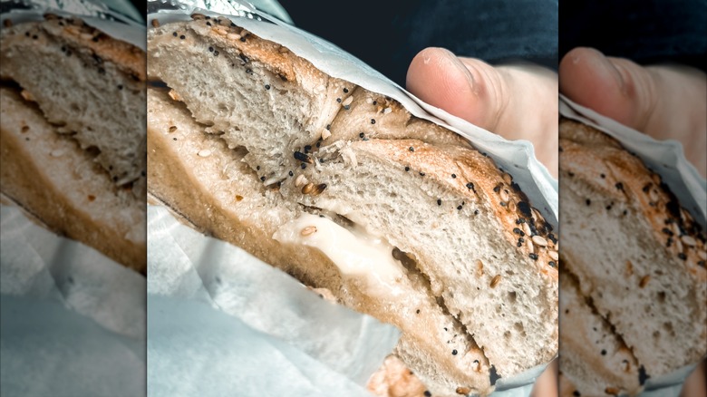 A close up of a New York style bagel that has butter in it and the bagel is wrapped in plastic wrap