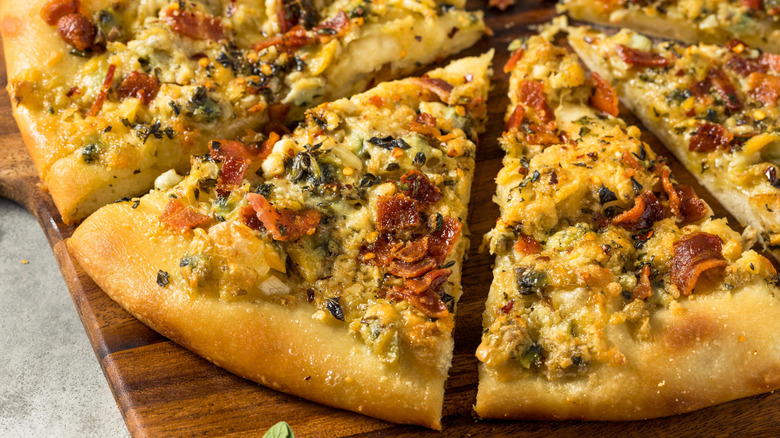 S﻿﻿﻿﻿lices of white clam pizza served on a wooden board. The crust is golden and topped with chopped clams, garlic, herbs, and bits of bacon