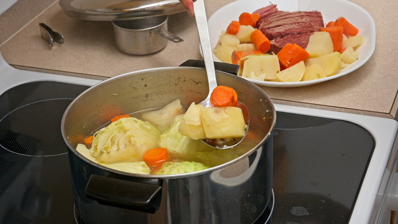 Spoon ladling boiled potatoes and carrots from pot