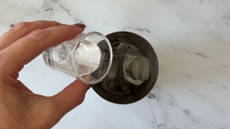 Hand pouring clear liquor into cocktail shaker