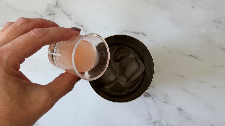 Hand pouring grapefruit juice into cocktail shaker