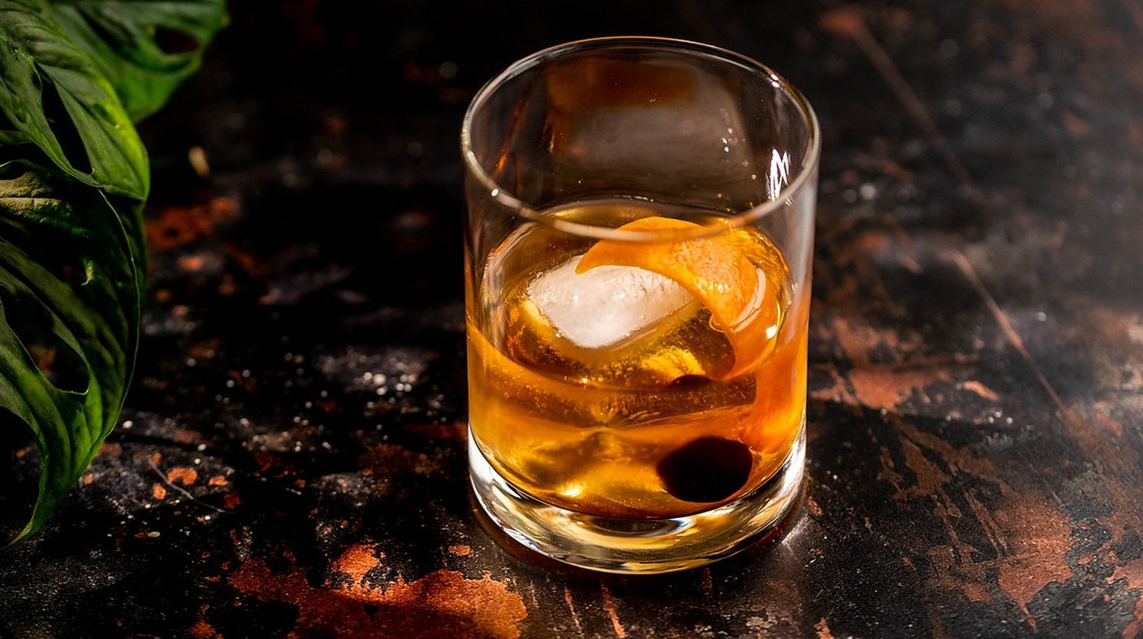 An old fashioned in a lowball glass with a large ice cube and an orange  peel