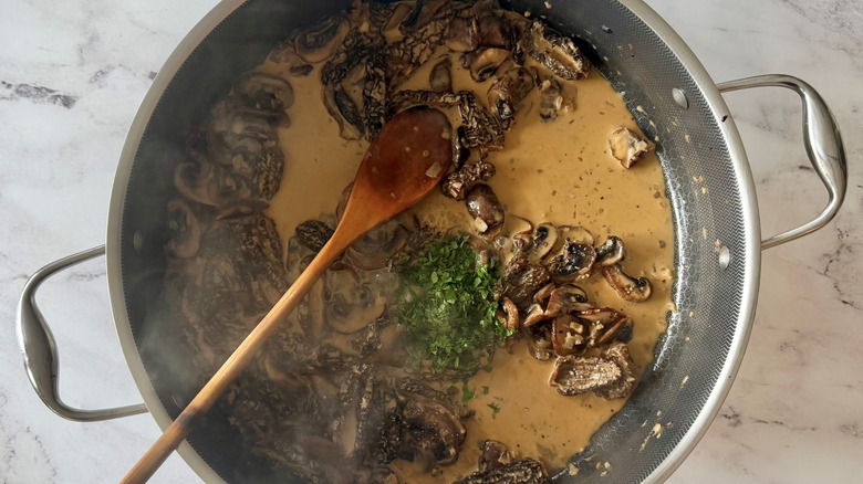 Wooden spoon in skillet with creamy mushroom sauce and parsley