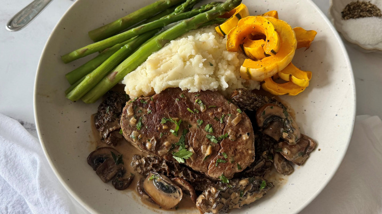 Steak Diane serving with mashed potatoes, asparagus, and squash