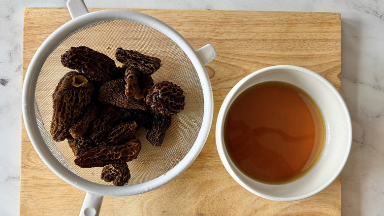 Morel mushrooms in strainer next to soaking liquid in bowl
