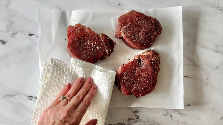 Hand patting steaks dry with paper towel