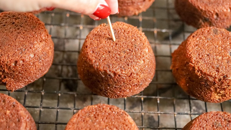 Hand poking toothpick into sticky toffee pudding muffin on wire rack