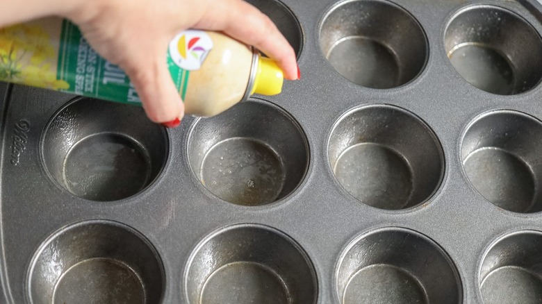 Hand spraying muffin tin with cooking spray