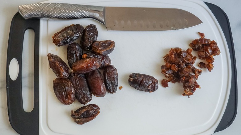 Whole and chopped dates on cutting board with knife