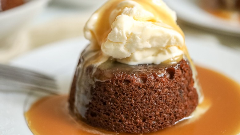 Sticky toffee pudding serving on plate with ice cream and toffee sauce