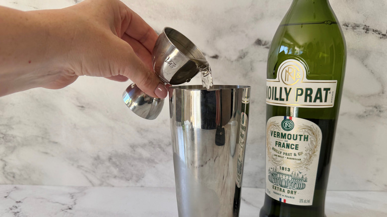 Hand pouring vermouth into cocktail shaker