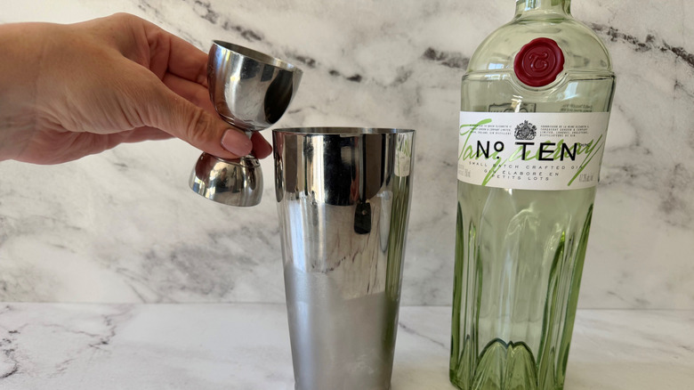 Hand pouring jigger with gin into cocktail shaker