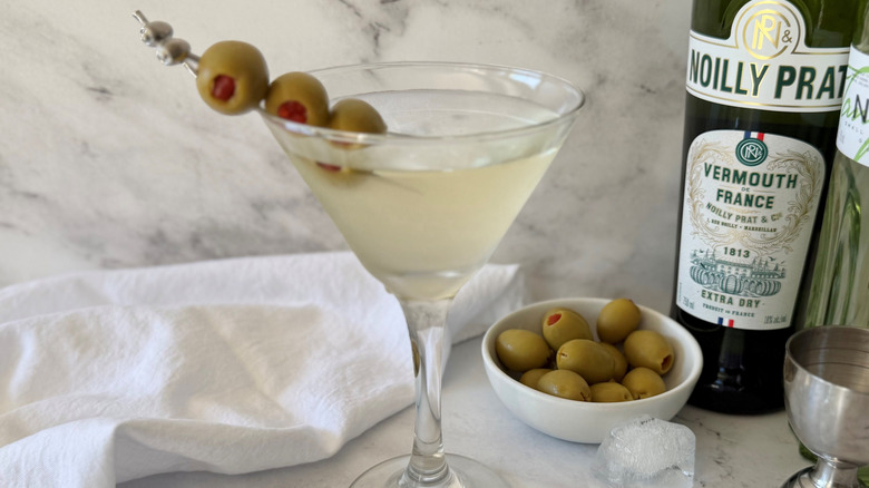 Martini with olive garnish next to liquor bottles