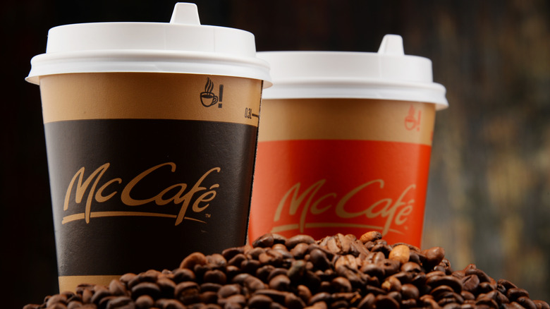 Two McCafe to-go cups sitting behind a mound of coffee beans