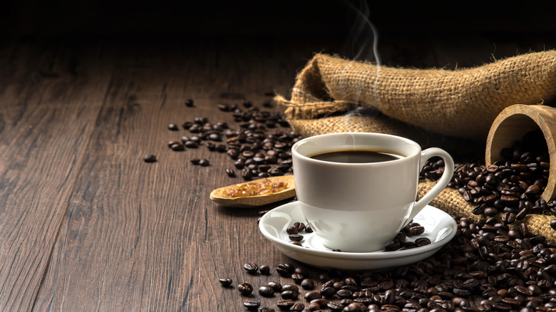 Cup of coffee in saucer next to sack of beans