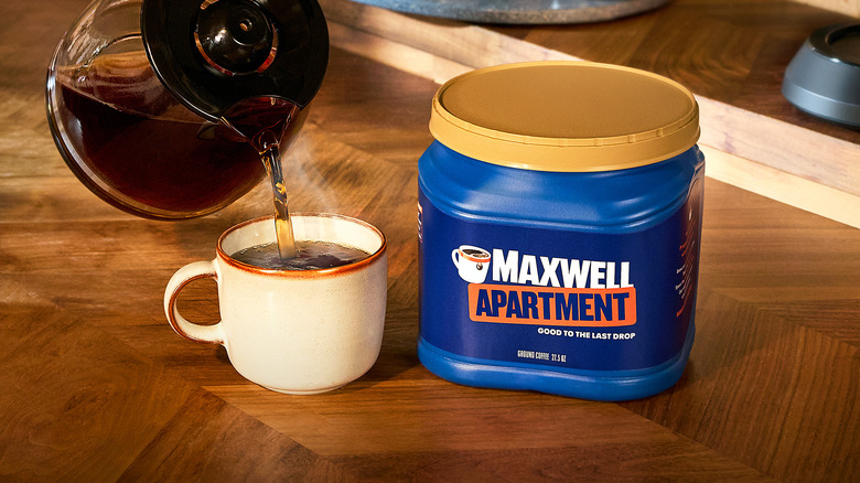 Blue "Maxwell Apartment" container next to carafe pouring coffee into mug