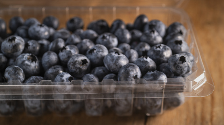 blueberries in a plastic clamshell container on a wooden table