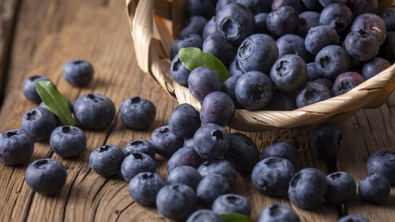 Container of blueberries spilling out onto a wooden surface
