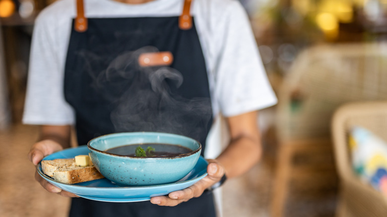 waiter carrying steaming bowl of soup