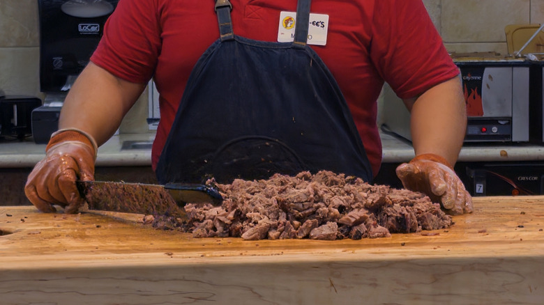 Buc-ee's employee chopping brisket on butcher block.
