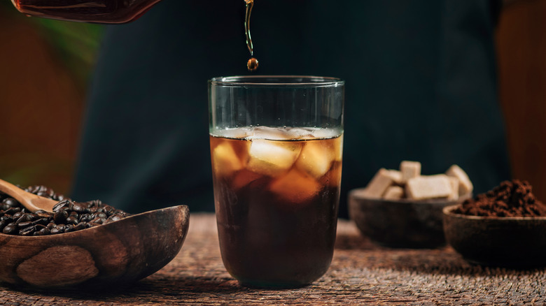 Glass of iced coffee on counter with bowls of coffee beans and grounds.