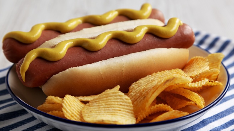 Two hot dogs with mustard and chips on a plate